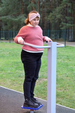 Tombul kız dışarıda sokak simülatörlerinde spor egzersizleri yapıyor.