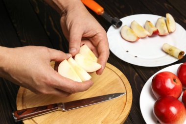 Yakın plan, ellerinde sulu elma dilimleri, arka planda bütün ve dilimlenmiş kırmızı elmalarla ahşap masada.
