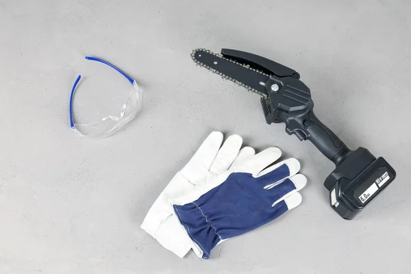 Tragbare Elektrische Kettensäge Mit Handschuhen Und Schutzbrille Auf Grauer Oberfläche — Stockfoto