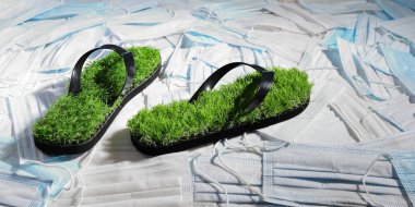 Gezegeni kirleten tek kullanımlık tıbbi maskelerin üzerinde taklit çimenler olan yeşil terlikler. Çevresel sorunlar kavramı