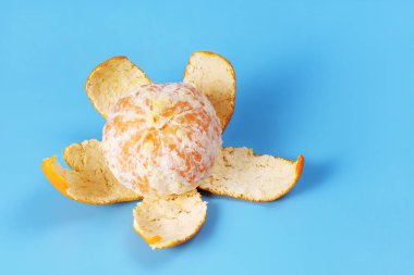 Orange round tangerine with separated leather under it, on blue background with copy space