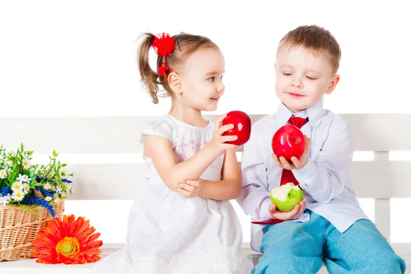 Boy and girl sitting on a bench with red apples — Stock Photo, Image