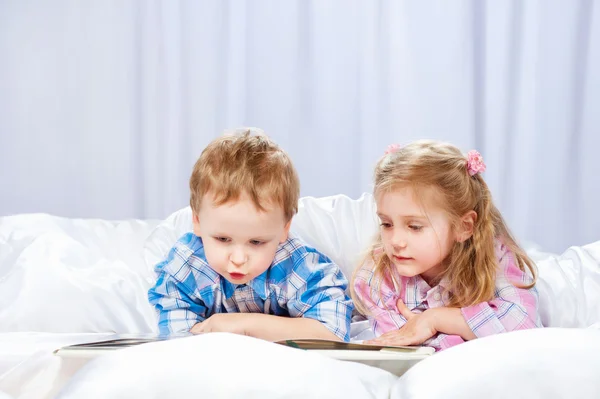 Menina e menino lêem o livro na cama — Fotografia de Stock