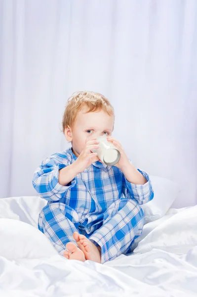 Garçon en pyjama buvant du lait, assis sur le lit — Photo