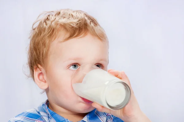 Ragazzo in pigiama che beve latte, su sfondo grigio — Foto Stock