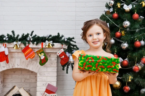 Kleines Mädchen mit einem Geschenk in der Nähe des Weihnachtsbaums — Stockfoto