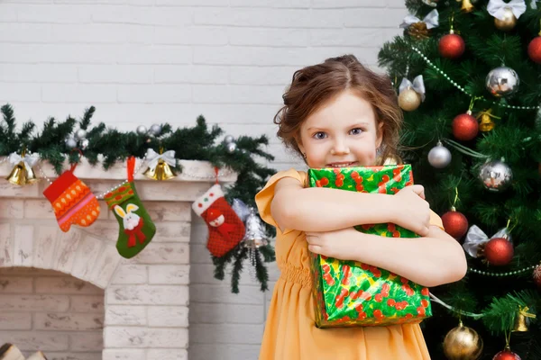 Kleines Mädchen mit einem Geschenk in der Nähe des Weihnachtsbaums — Stockfoto