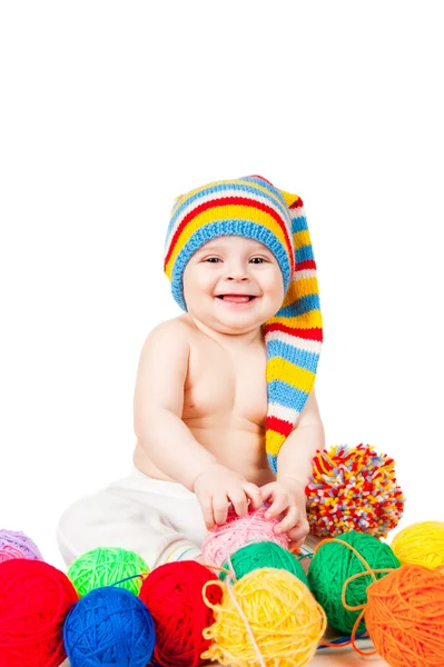 Smiling baby in a hat plays with balls of yarn — Stok fotoğraf