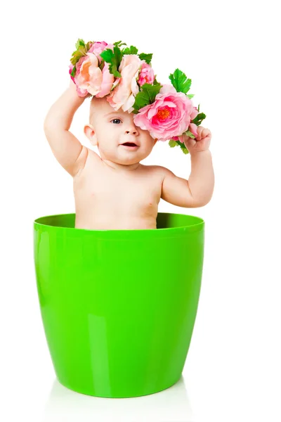 Ребенок в венке сидит в цветочном горшке, на сиреневом фоне — стоковое фото