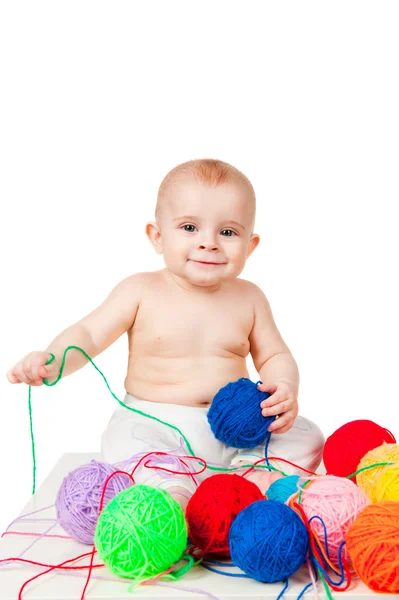 Улыбающийся ребенок играет с цветными клубками пряжи — стоковое фото