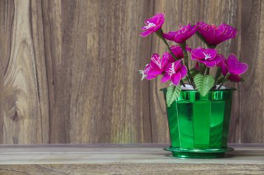 Tahta bir masanın üzerine yerleştirilmiş vazodaki sahte çiçekler, ahşap tahıl mahsulü arka plan tasarımı için fotokopi alanı..