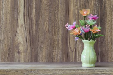 Tahta bir masanın üzerine yerleştirilmiş vazodaki sahte çiçekler, ahşap tahıl mahsulü arka plan tasarımı için fotokopi alanı..