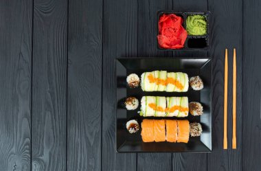 Siyah bir tabakta lezzetli suşi, siyah bir tahta üzerinde uzanır.