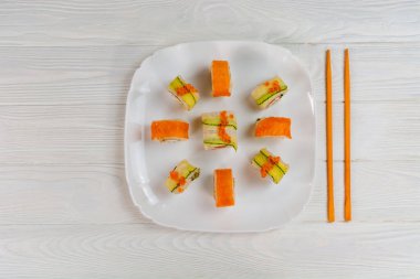 Suşi beyaz tahta arka planda beyaz bir tabak üzerine kurulmuş. Beyaz dokuma tahtasında lezzetli suşi..