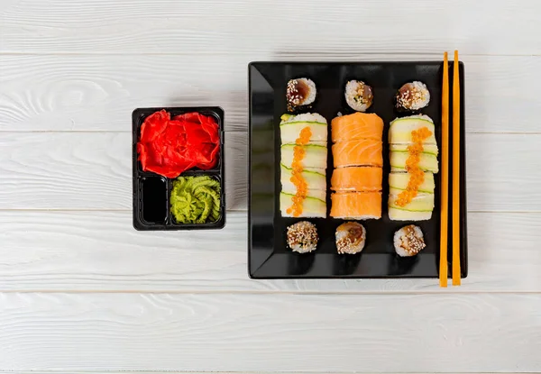 白色质感板上的美味寿司。寿司放在一个黑色的盘子上，白色的木制背景. — 图库照片
