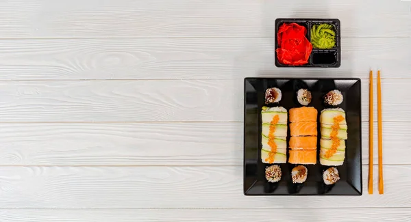 白色质感板上的美味寿司。寿司放在一个黑色的盘子上，白色的木制背景. — 图库照片