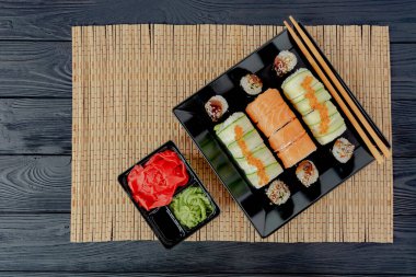 Bambu masa örtüsü üzerinde siyah desenli bir tahtada lezzetli suşi. Siyah bir tabakta lezzetli suşi, siyah bir tahta üzerinde uzanır.