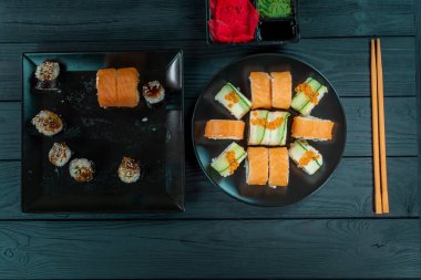 Siyah bir tabakta lezzetli suşi, siyah bir tahta üzerinde uzanır. Suşi takımlı siyah tahta..