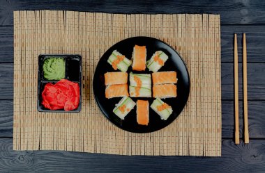 Siyah ahşap arka planda somonlu suşi rulosu. Japon mutfağı. Suşi menüsü. Suşi Philadelphia 'yı bambu masa örtüsüne sardı.. 