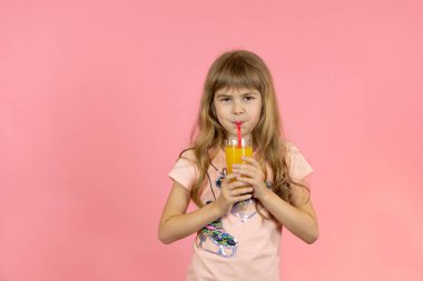 Küçük kız pembe arka planda portakal suyu içiyor. Pembe arka planda elinde portakal tutan bir kız.