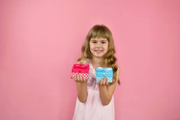 女の子は陽気にピンクの背景にポーズ ピンクのドレスを着た女の子が手に贈り物を持っている メリー誕生日の女の子 — ストック写真