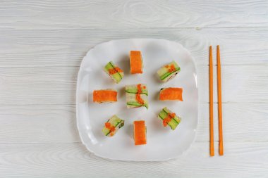 Suşi beyaz tahta arka planda beyaz bir tabak üzerine kurulmuş. Beyaz dokuma tahtasında lezzetli suşi..