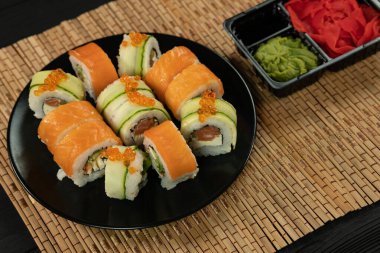 Siyah ahşap arka planda somonlu suşi rulosu. Japon mutfağı. Suşi menüsü. Suşi Philadelphia 'yı bambu masa örtüsüne sardı.. 