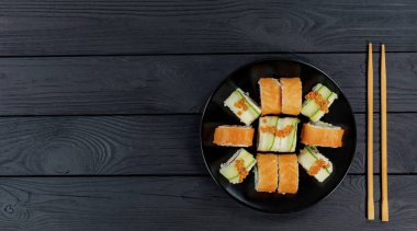 Siyah bir tabakta lezzetli suşi, siyah bir tahta üzerinde uzanır. Suşi takımlı siyah tahta..