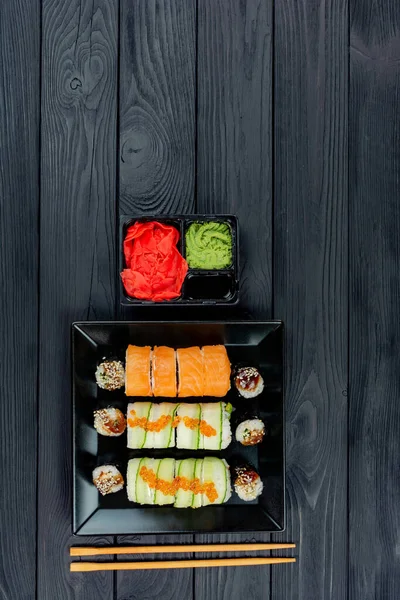 Läcker sushi på en svart tallrik, ligg på en svart träskiva. — Stockfoto