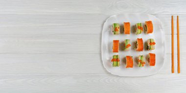 Suşi beyaz tahta arka planda beyaz bir tabak üzerine kurulmuş. Beyaz dokuma tahtasında lezzetli suşi..