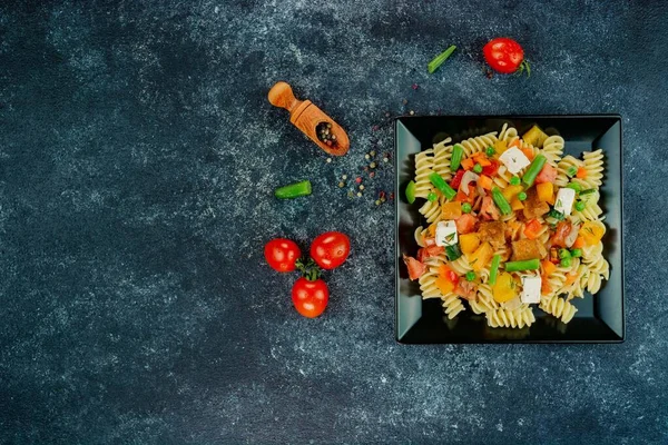 Sebzeli makarna, kuşkonmaz, bezelye, dolmalık biber, domates, sos, siyah arkaplanda mozzarella peyniri. Sebzeli İtalyan makarnası ve koyu bir arka planda baharat. Anlaşıldı..