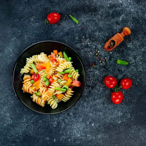 Sebzeli makarna, kuşkonmaz, bezelye, dolmalık biber, domates, sos, siyah arkaplanda mozzarella peyniri. Sebzeli İtalyan makarnası ve koyu bir arka planda baharat. Anlaşıldı..