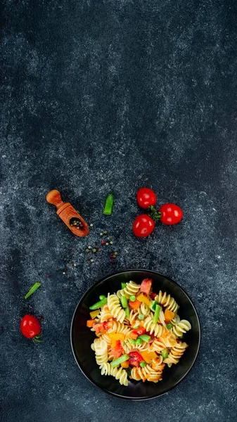 Sebzeli makarna, kuşkonmaz, bezelye, dolmalık biber, domates, sos, siyah arkaplanda mozzarella peyniri. Sebzeli İtalyan makarnası ve koyu bir arka planda baharat. Anlaşıldı..