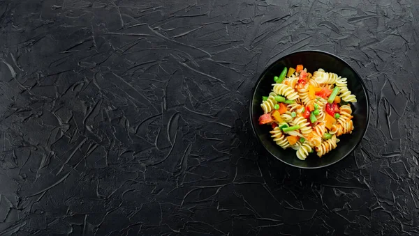 Sebzeli makarna, kuşkonmaz, bezelye, dolmalık biber, domates, sos, siyah arkaplanda mozzarella peyniri. Sebzeli İtalyan makarnası ve koyu bir arka planda baharat. Anlaşıldı..