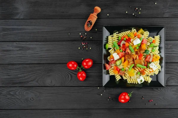 Sebzeli makarna, bezelye, tatlı biber, domates, sos, siyah ahşap arka planda mozzarella peyniri. Arka planda sebze ve baharatlı İtalyan makarnası. Anlaşıldı..