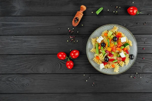 Sebzeli makarna, bezelye, tatlı biber, domates, sos, siyah ahşap arka planda mozzarella peyniri. Arka planda sebze ve baharatlı İtalyan makarnası. Anlaşıldı..