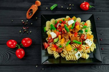 Sebzeli makarna, bezelye, tatlı biber, domates, sos, siyah ahşap arka planda mozzarella peyniri. Karanlık bir arka planda sebzeli ve baharatlı İtalyan makarnası..