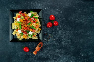 Sebzeli makarna, kuşkonmaz, bezelye, dolmalık biber, domates, sos, siyah arkaplanda mozzarella peyniri. Sebzeli İtalyan makarnası ve arka planda baharat..