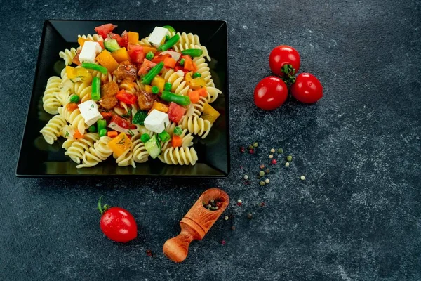 Sebzeli makarna, kuşkonmaz, bezelye, dolmalık biber, domates, sos, siyah arkaplanda mozzarella peyniri. Sebzeli İtalyan makarnası ve arka planda baharat..