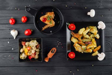 Mantarlı kızarmış patates ve baharatlı siyah arka planda domates. Sebzeli lezzetli patates ve siyah panoda kızarmış tavuk. Sebze ve patatesli kızarmış tavuk..