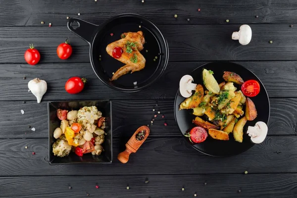 Mantarlı kızarmış patates ve baharatlı siyah arka planda domates. Sebzeli lezzetli patates ve siyah panoda kızarmış tavuk. Sebze ve patatesli kızarmış tavuk..