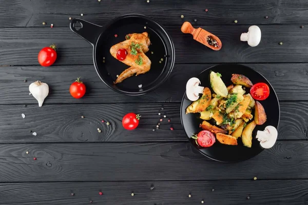 Mantarlı kızarmış patates ve baharatlı siyah arka planda domates. Sebzeli lezzetli patates ve siyah panoda kızarmış tavuk. Sebze ve patatesli kızarmış tavuk..