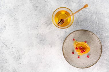 Hafif beton arka planda ballı krepler. Elim, balı döken ahşap bir sopa tutuyor..