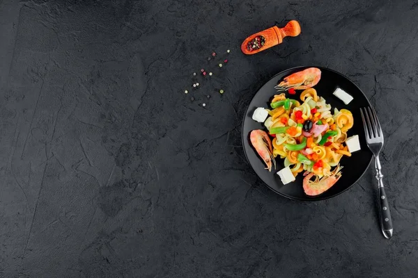 Siyah beton arka planda karidesli çok renkli makarna. Siyah tabakta İtalyan makarnası servis ediyorum..