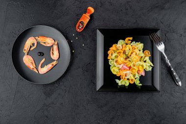 Siyah beton arka planda karidesli çok renkli makarna. Siyah tabakta İtalyan makarnası servis ediyorum..