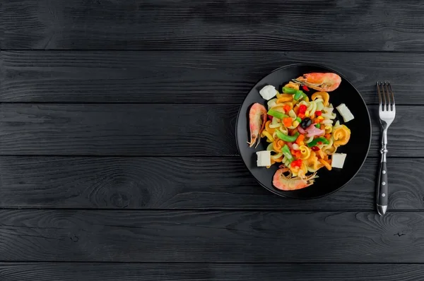 Multicolored pasta with shrimps on a black wooden background. Serving a dish of Italian pasta on a black plate.