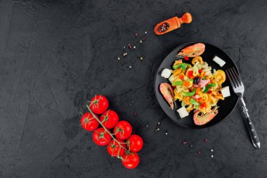 Siyah beton arka planda karidesli çok renkli makarna. Siyah tabakta İtalyan makarnası servis ediyorum..