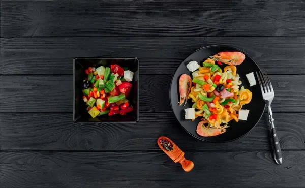 Siyah ahşap arka planda karidesli çok renkli makarna. Siyah tabakta İtalyan makarnası servis ediyorum..