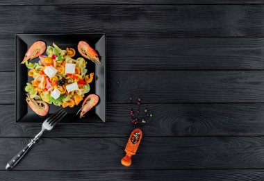 Siyah ahşap arka planda karidesli çok renkli makarna. Siyah tabakta İtalyan makarnası servis ediyorum..