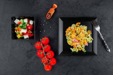 Siyah beton arka planda çok renkli makarna. Düz yatıyordu. Üst Manzara. Çok renkli farfalle, seçici odaklı, stüdyoda çekilmiş siyah bir kase..